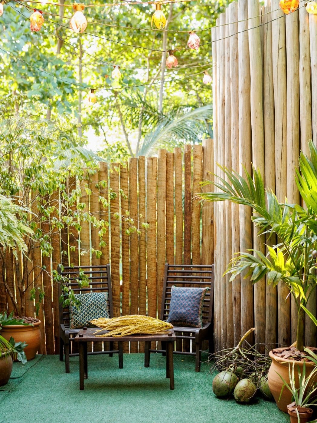 Quintal com cadeiras de madeira, plantas tropicais e luzes coloridas penduradas — atmosfera de Caraíva