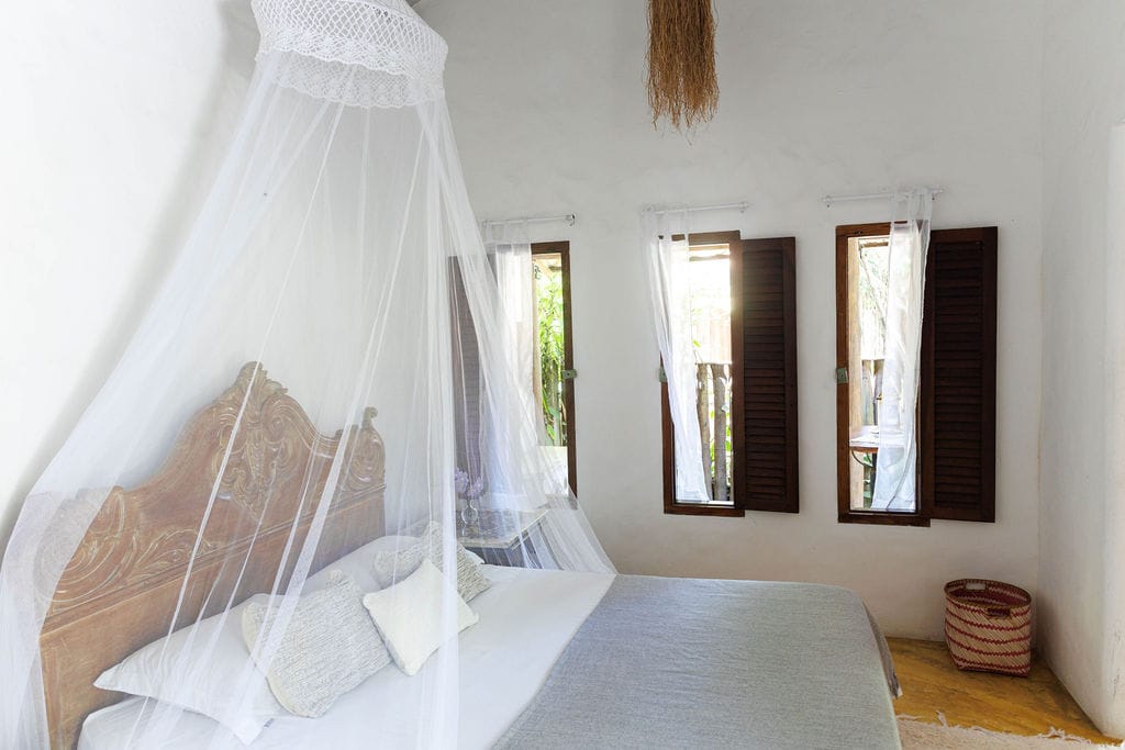 Quarto da Vila Bahia com dossel branco e janelas de madeira